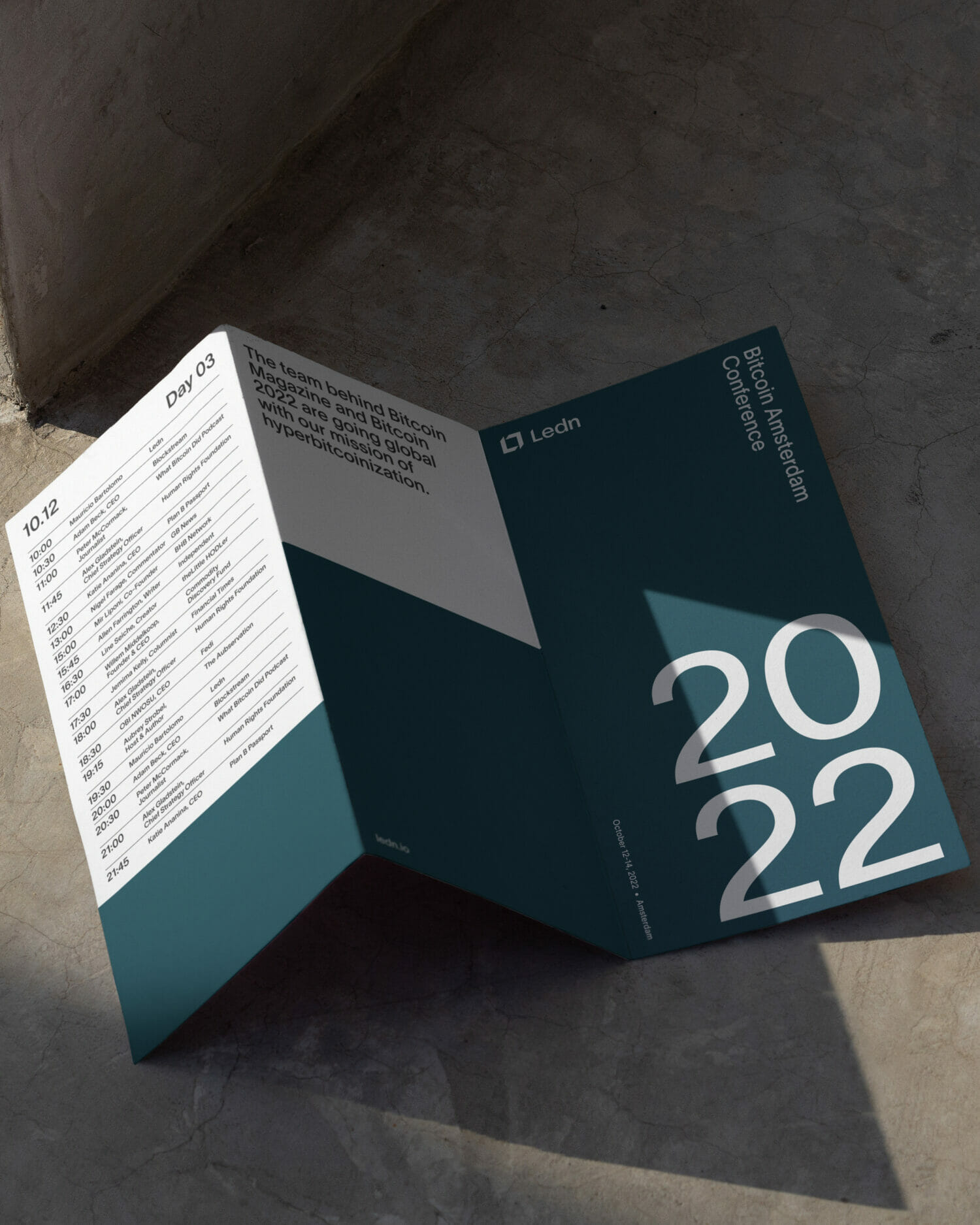 Folded conference brochure for Ledn displayed in dramatic natural light, featuring the Bitcoin Amsterdam Conference 2022 schedule, minimalist typography, and refined branding focused on modern digital finance.