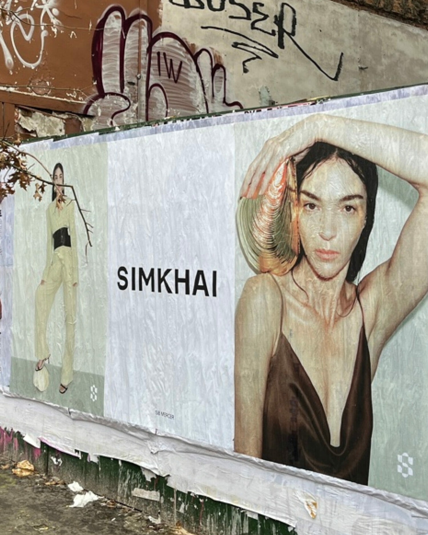 Simkhai fashion posters displayed on an wall with graffiti, featuring 2 portraits of model and minimalist campaign styling.