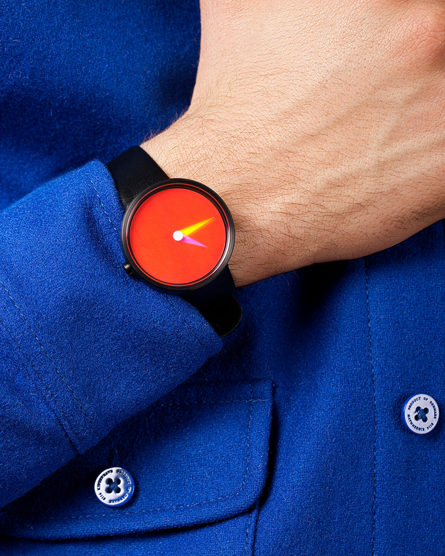 Person wearing the watch from moma design store with a bright orange dial and black strap against a blue garment.