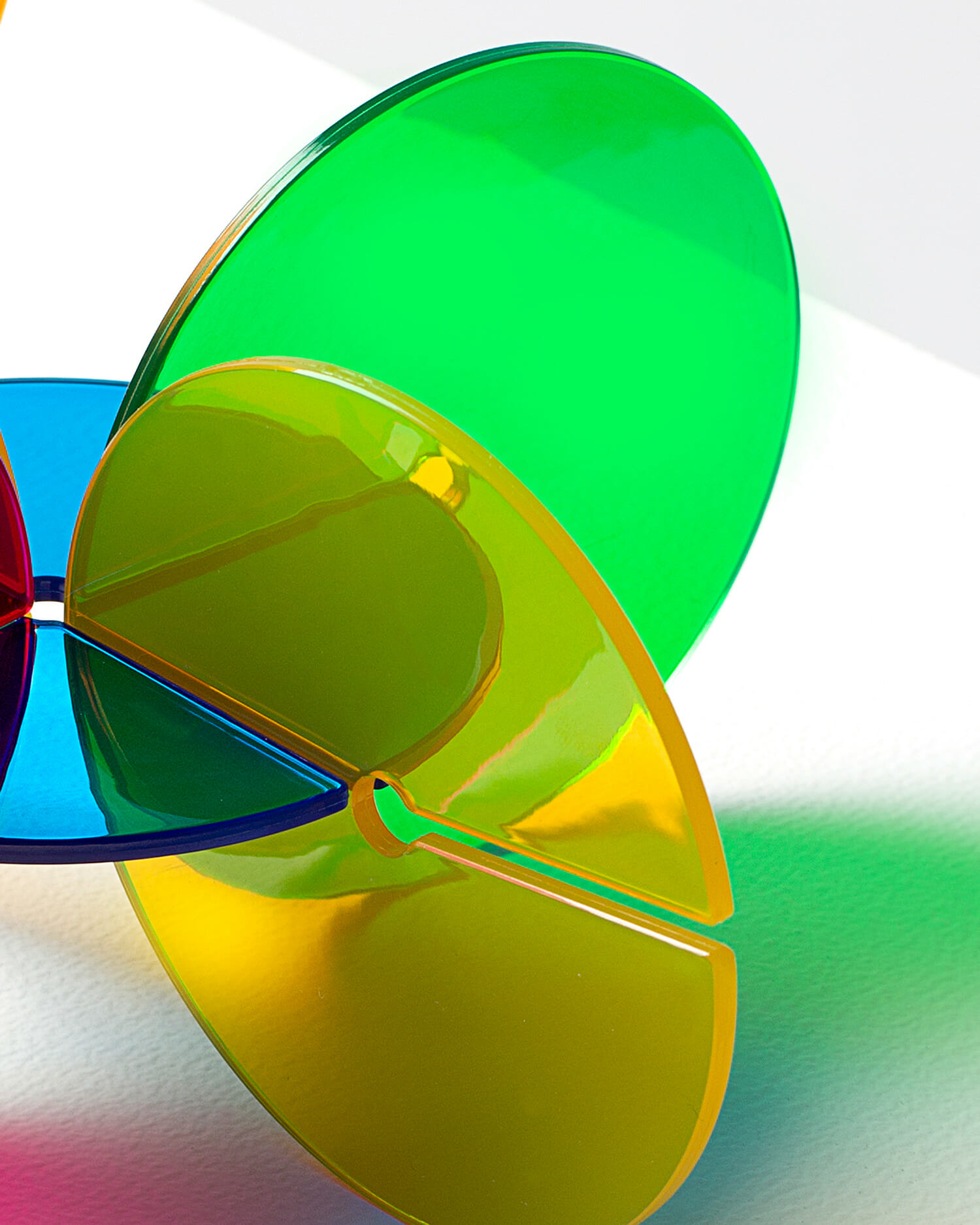 Overlapping translucent green, yellow, blue, and red acrylic coaster pieces creating colorful reflections