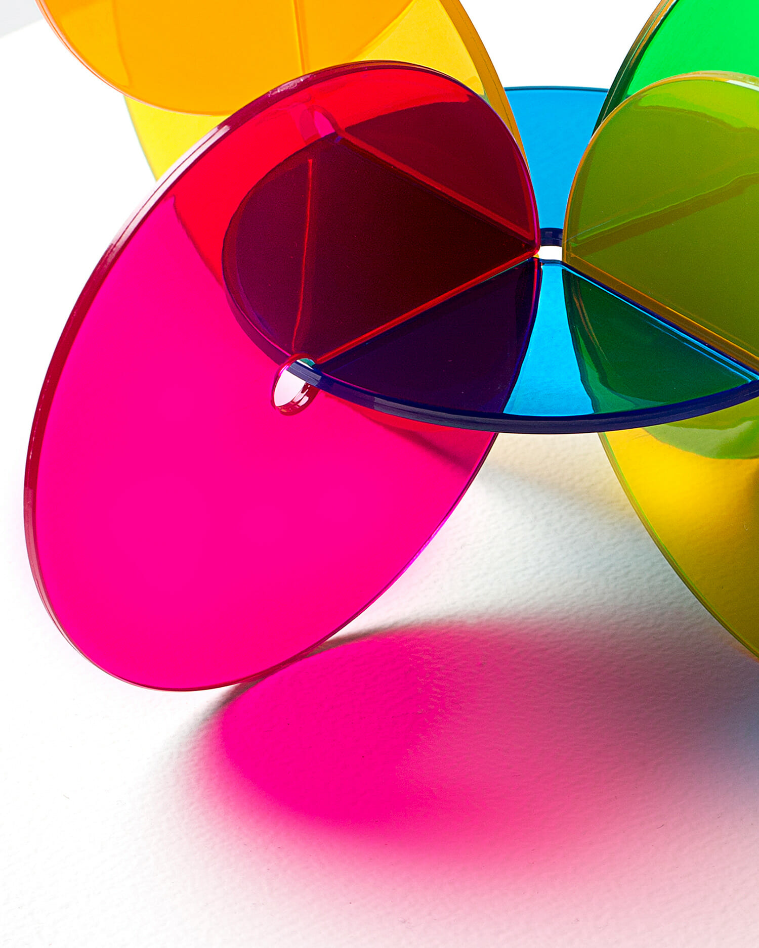 Translucent pink, red, blue, yellow, and green coaster pieces arranged in an overlapping circular design with colorful shadows