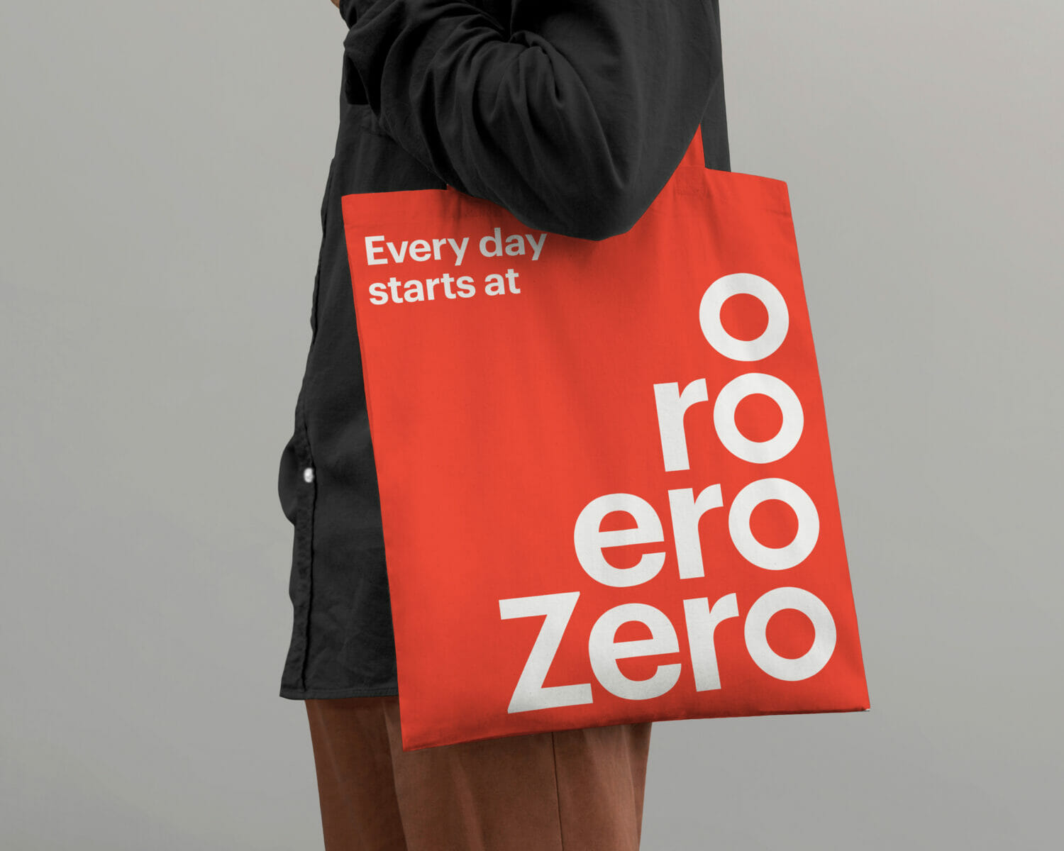 Person carrying a coral red Zero branded tote bag with the text Every day starts at and the Zero wordmark