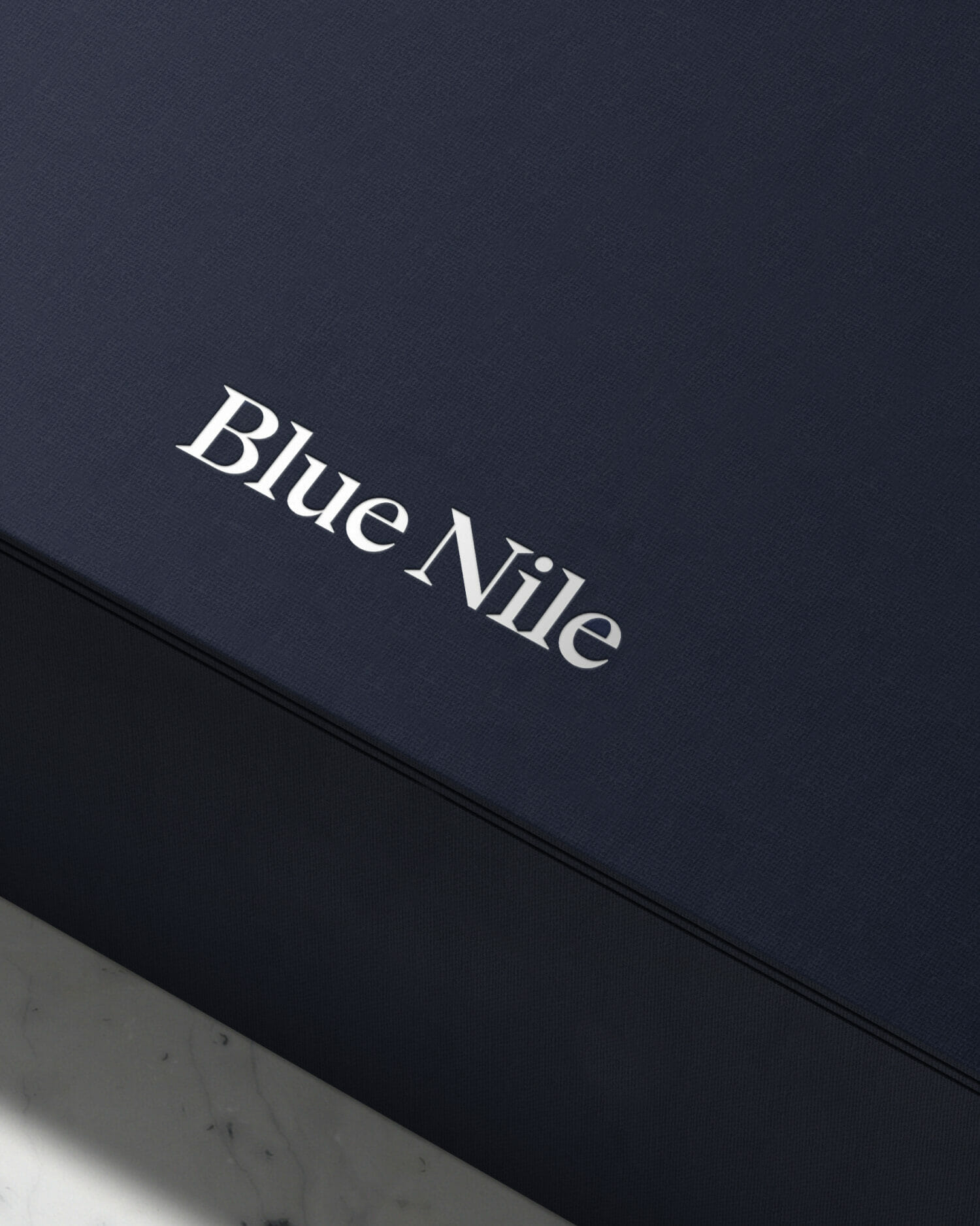 Blue nile logo embossed on a textured navy jewelry box, highlighting premium packaging craftsmanship.