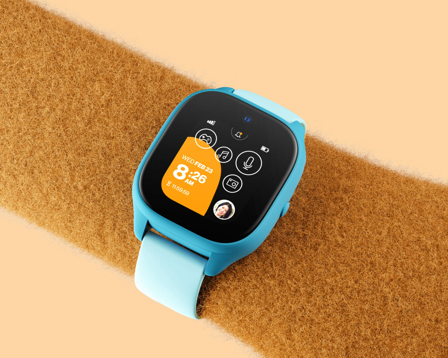 Verizon Ggzmo smartwatch worn on a fuzzy orange arm, displaying the colorful home screen and communication features for kids.